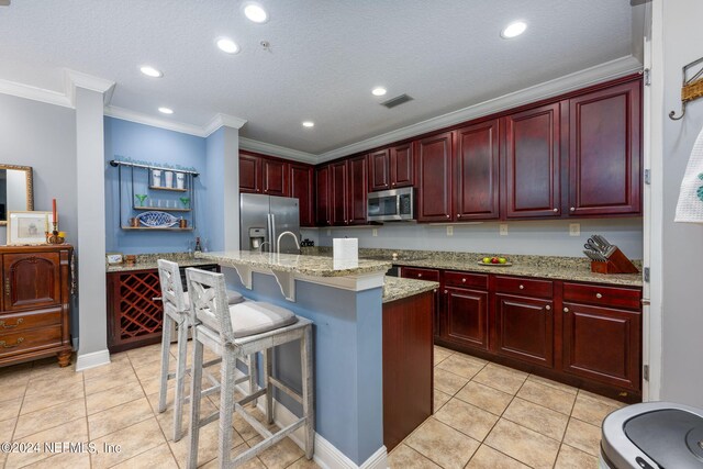 kitchen featuring appliances with stainless steel finishes, a breakfast bar, light tile patterned floors, crown molding, and a kitchen island with sink