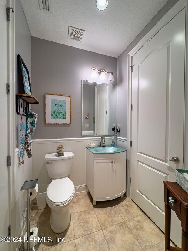 bathroom featuring vanity, toilet, a textured ceiling, and tile patterned floors