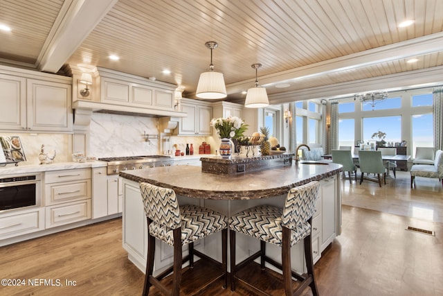 kitchen featuring an island with sink, stainless steel appliances, hardwood / wood-style floors, and decorative light fixtures