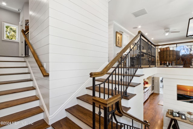 staircase with wood-type flooring, wooden walls, and ceiling fan