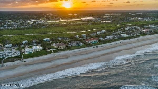 aerial view at dusk featuring a view of the beach and a water view