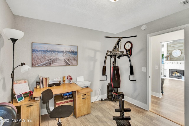 office space with visible vents, baseboards, a lit fireplace, a textured ceiling, and light wood-style floors