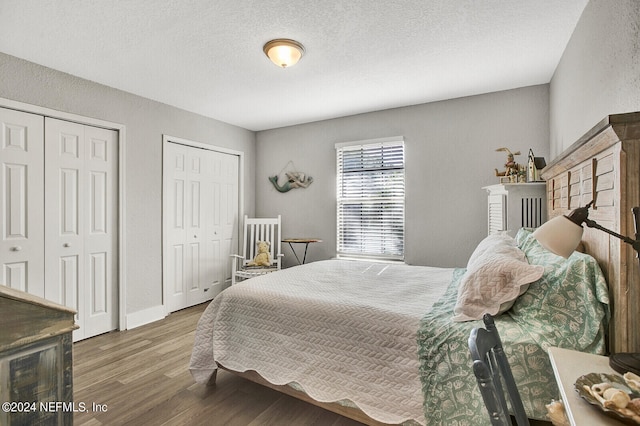 bedroom featuring multiple closets, a textured ceiling, baseboards, and wood finished floors