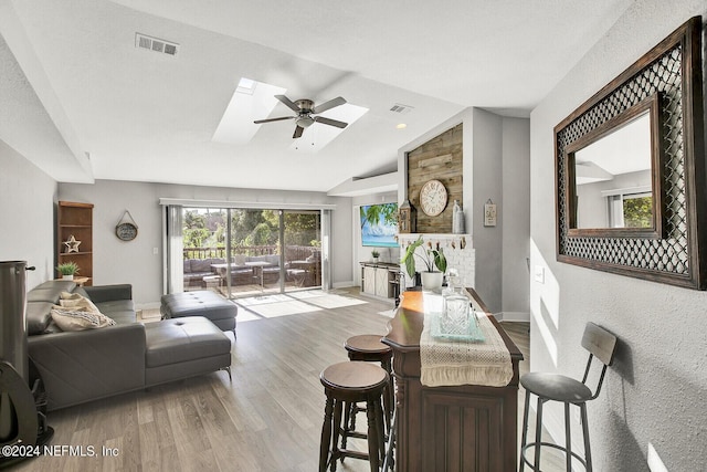 living area with baseboards, vaulted ceiling with skylight, visible vents, and wood finished floors