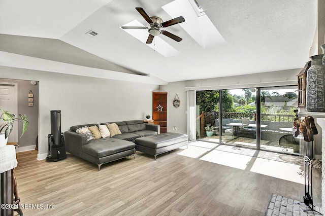 living room featuring light wood-style floors, vaulted ceiling with skylight, visible vents, and ceiling fan