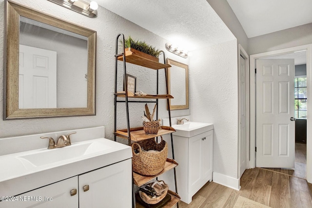 full bathroom featuring a textured wall, two vanities, a sink, and wood finished floors