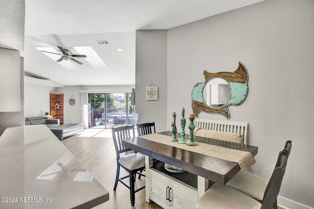 dining space featuring a ceiling fan, visible vents, a textured wall, and light wood-style flooring