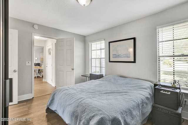 bedroom with baseboards, wood finished floors, and a textured wall