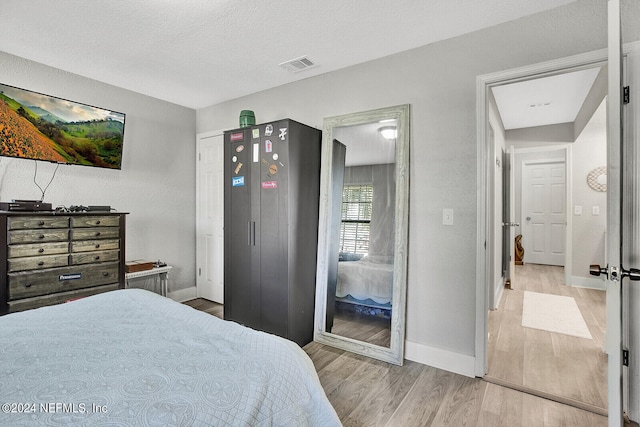 bedroom featuring visible vents, a textured ceiling, baseboards, and wood finished floors