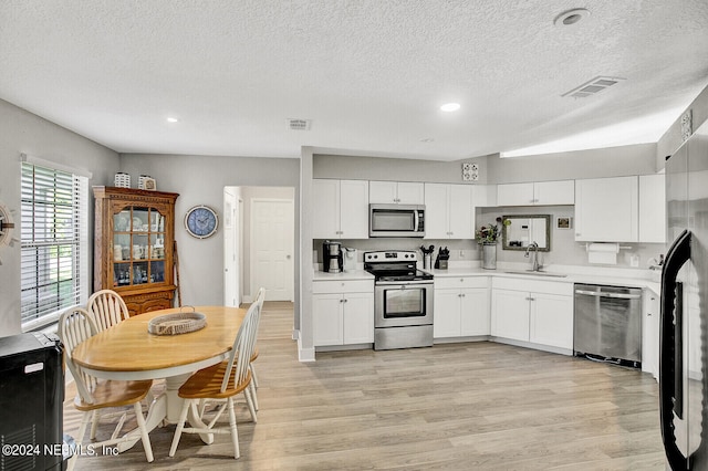 kitchen with stainless steel appliances, a sink, white cabinets, light countertops, and light wood-type flooring