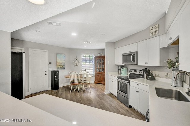 kitchen featuring wood finished floors, stainless steel appliances, light countertops, white cabinetry, and a sink