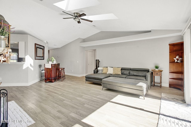 living room with vaulted ceiling with skylight, ceiling fan, baseboards, and wood finished floors