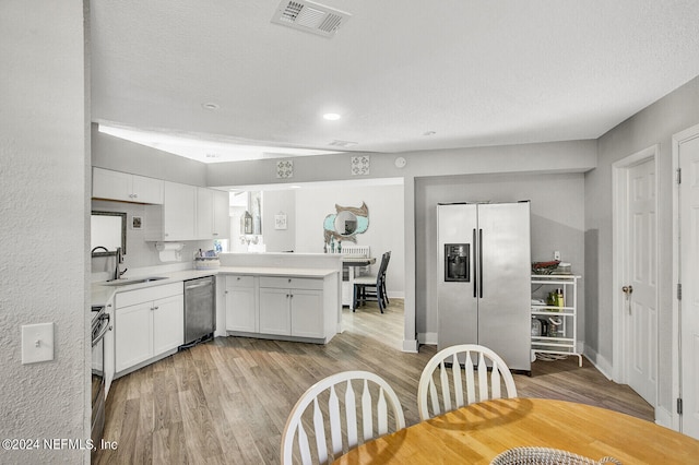 kitchen featuring visible vents, a peninsula, stainless steel appliances, light countertops, and a sink