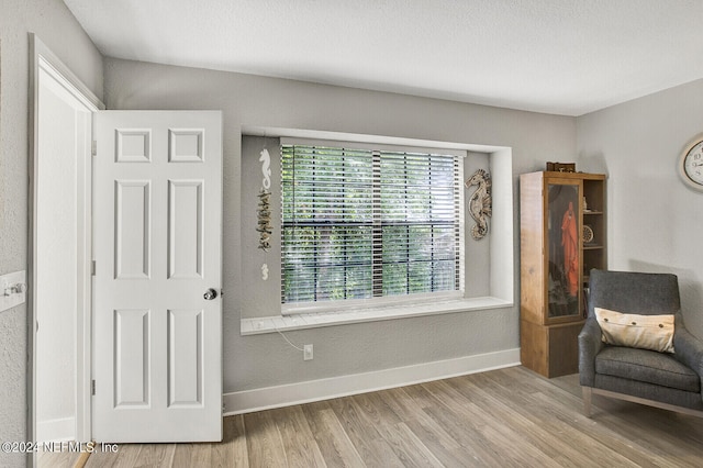 sitting room with a textured ceiling, a textured wall, wood finished floors, and baseboards