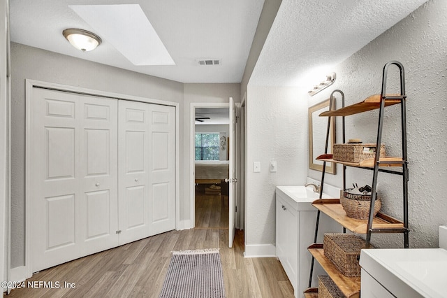 ensuite bathroom featuring two vanities, visible vents, a textured wall, and wood finished floors