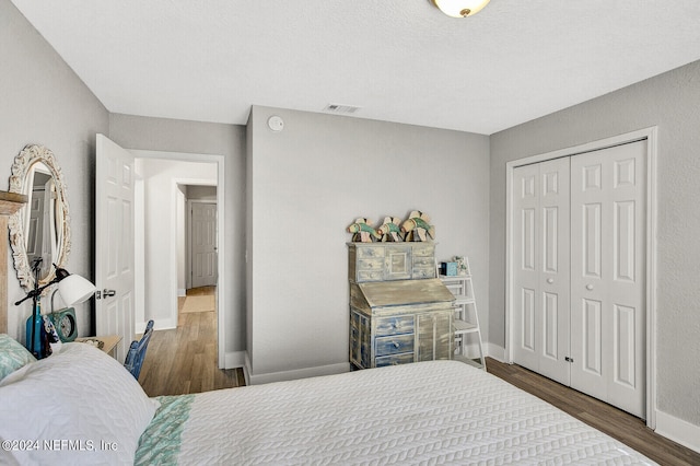 bedroom with a closet, wood finished floors, visible vents, and baseboards