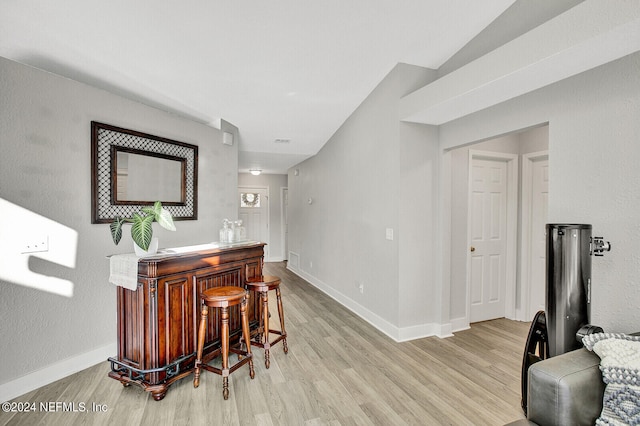 bar with a bar, light wood-type flooring, and baseboards