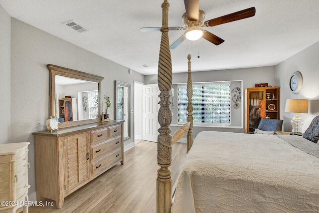 bedroom featuring light wood-style floors, ceiling fan, visible vents, and a textured ceiling