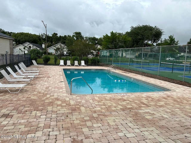 pool with a tennis court, a patio, and fence