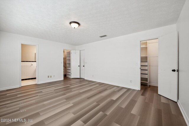 unfurnished bedroom featuring a textured ceiling, wood-type flooring, a closet, a walk in closet, and ensuite bathroom