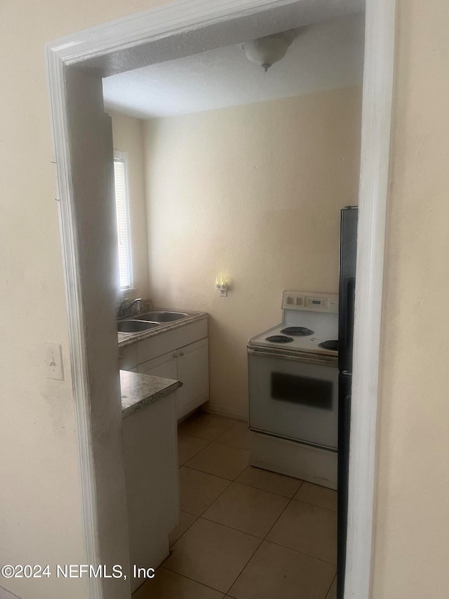 kitchen with white cabinets, light tile patterned floors, sink, and electric range