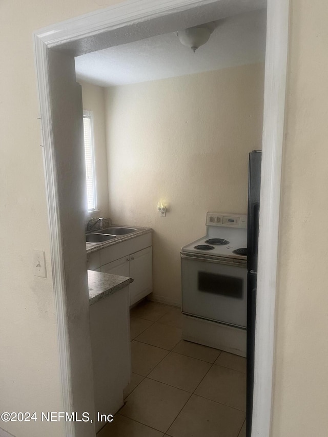 kitchen featuring white electric range oven, light tile patterned floors, freestanding refrigerator, a sink, and white cabinetry