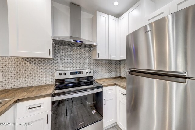 kitchen featuring wall chimney exhaust hood, wood counters, backsplash, appliances with stainless steel finishes, and white cabinetry