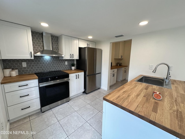 kitchen with appliances with stainless steel finishes, sink, white cabinetry, wooden counters, and wall chimney range hood