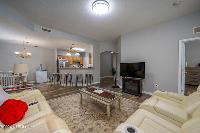 living area with wood finished floors, a textured ceiling, visible vents, arched walkways, and an inviting chandelier