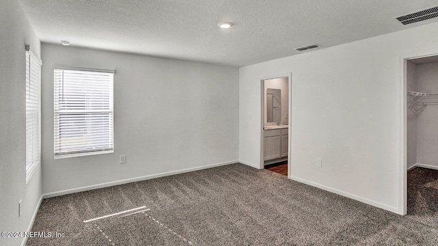 unfurnished bedroom with dark carpet, visible vents, a walk in closet, and a textured ceiling