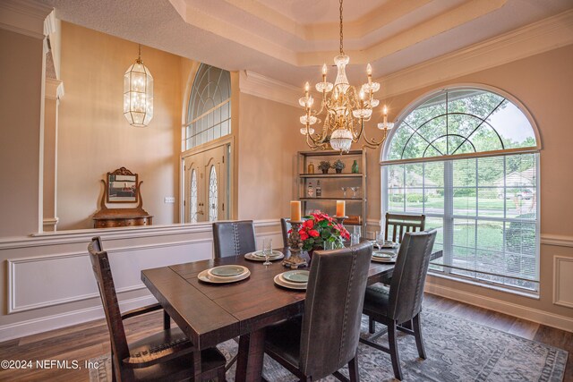 dining room featuring a raised ceiling, ornamental molding, a notable chandelier, and dark hardwood / wood-style flooring