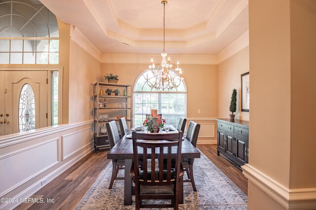 dining room with dark wood-type flooring, ornamental molding, a tray ceiling, and a notable chandelier