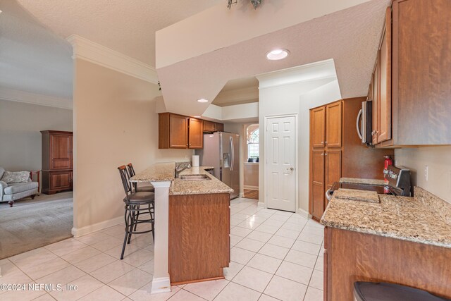 kitchen featuring a breakfast bar, light tile patterned floors, kitchen peninsula, stainless steel appliances, and light stone countertops