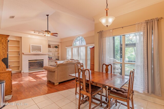 tiled dining area with built in features, a fireplace, lofted ceiling, ornamental molding, and ceiling fan