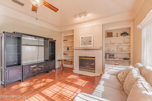 living room featuring hardwood / wood-style flooring, a fireplace, ornamental molding, built in shelves, and vaulted ceiling