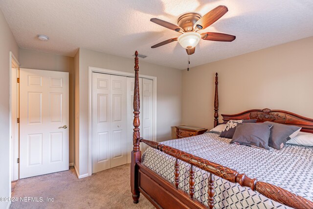 bedroom with ceiling fan, a closet, light carpet, and a textured ceiling