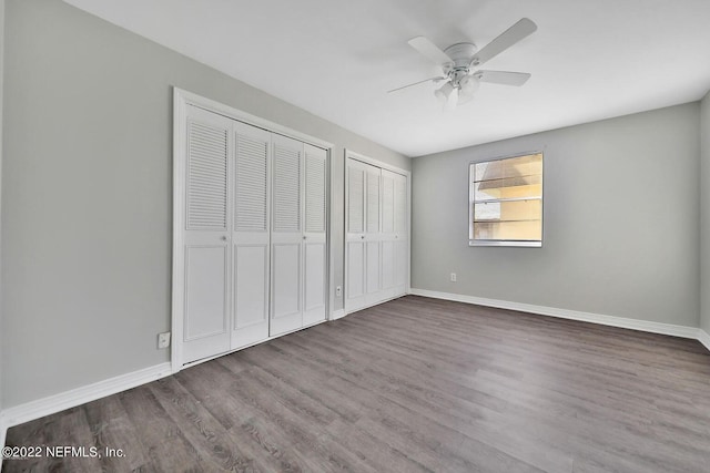 unfurnished bedroom with baseboards, wood finished floors, two closets, and ceiling fan