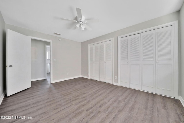 unfurnished bedroom with wood finished floors, multiple closets, baseboards, visible vents, and ceiling fan
