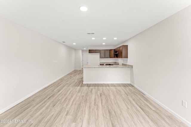 kitchen with light stone counters, light wood-type flooring, and kitchen peninsula