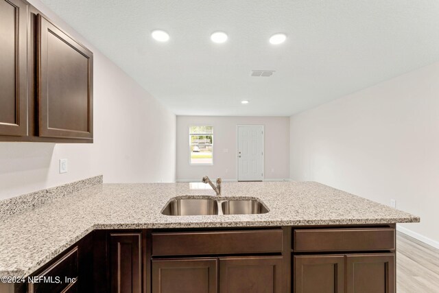 kitchen with light stone counters, light wood-type flooring, sink, and kitchen peninsula