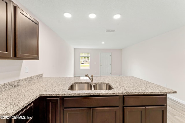 kitchen with a peninsula, visible vents, dark brown cabinets, and a sink