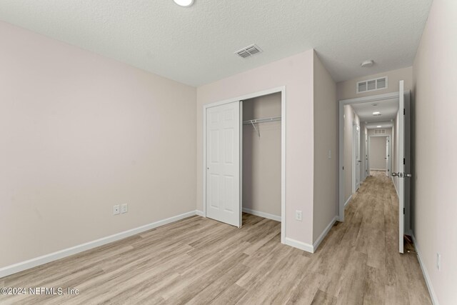 unfurnished bedroom with light hardwood / wood-style flooring, a closet, and a textured ceiling