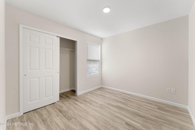 unfurnished bedroom with light wood-type flooring, a textured ceiling, baseboards, and a closet