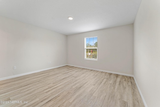 spare room with baseboards, a textured ceiling, and light wood finished floors