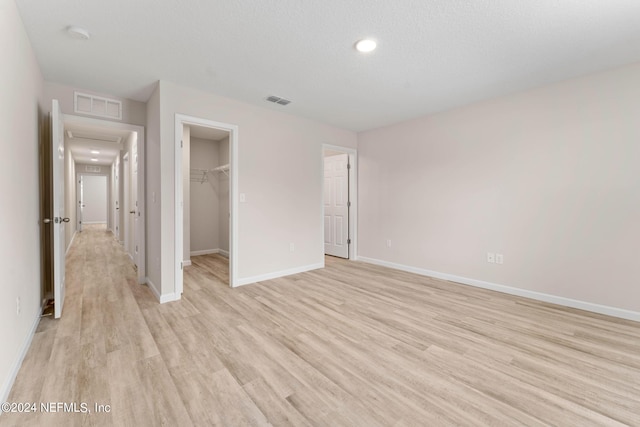 unfurnished bedroom with a textured ceiling, a closet, a spacious closet, and light hardwood / wood-style flooring