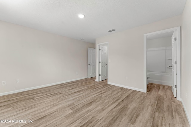 unfurnished bedroom featuring a textured ceiling, visible vents, baseboards, light wood-style floors, and ensuite bath