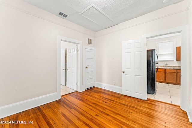 unfurnished bedroom with black refrigerator, a textured ceiling, ensuite bath, and light hardwood / wood-style flooring