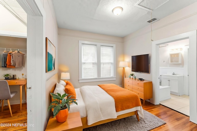 bedroom featuring a textured ceiling, light hardwood / wood-style flooring, ensuite bath, sink, and a closet