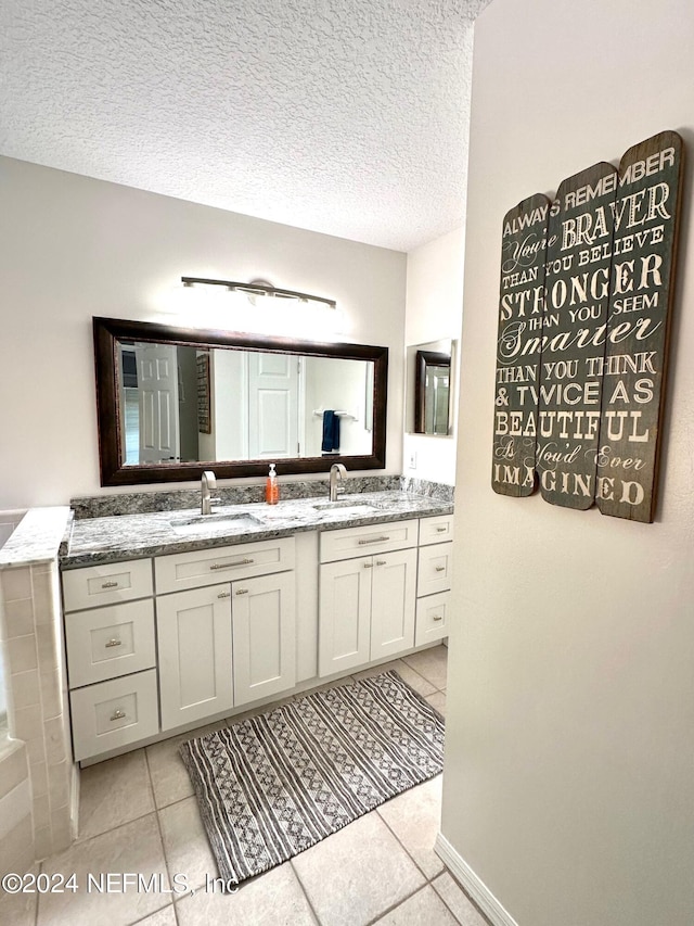 bathroom with a textured ceiling, double vanity, tile patterned flooring, and a sink