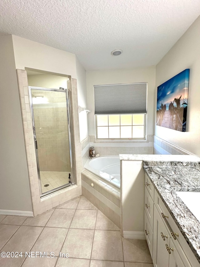 full bathroom featuring a textured ceiling, tile patterned flooring, vanity, a bath, and a stall shower